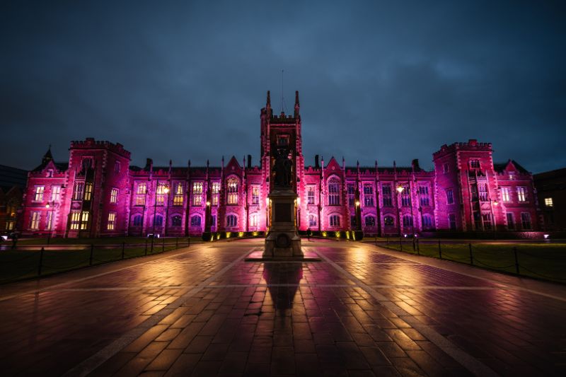 Front of the Lanyon Building light up in pink purple against a dark night sky.